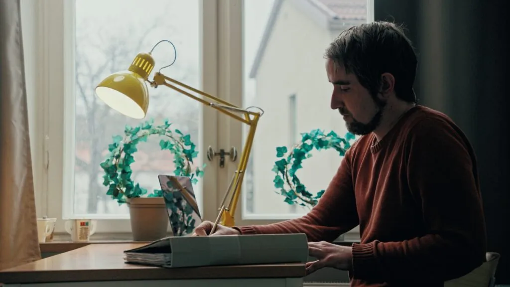 Man som sitter vid ett skrivbord med lampa och blommor i ett fönster