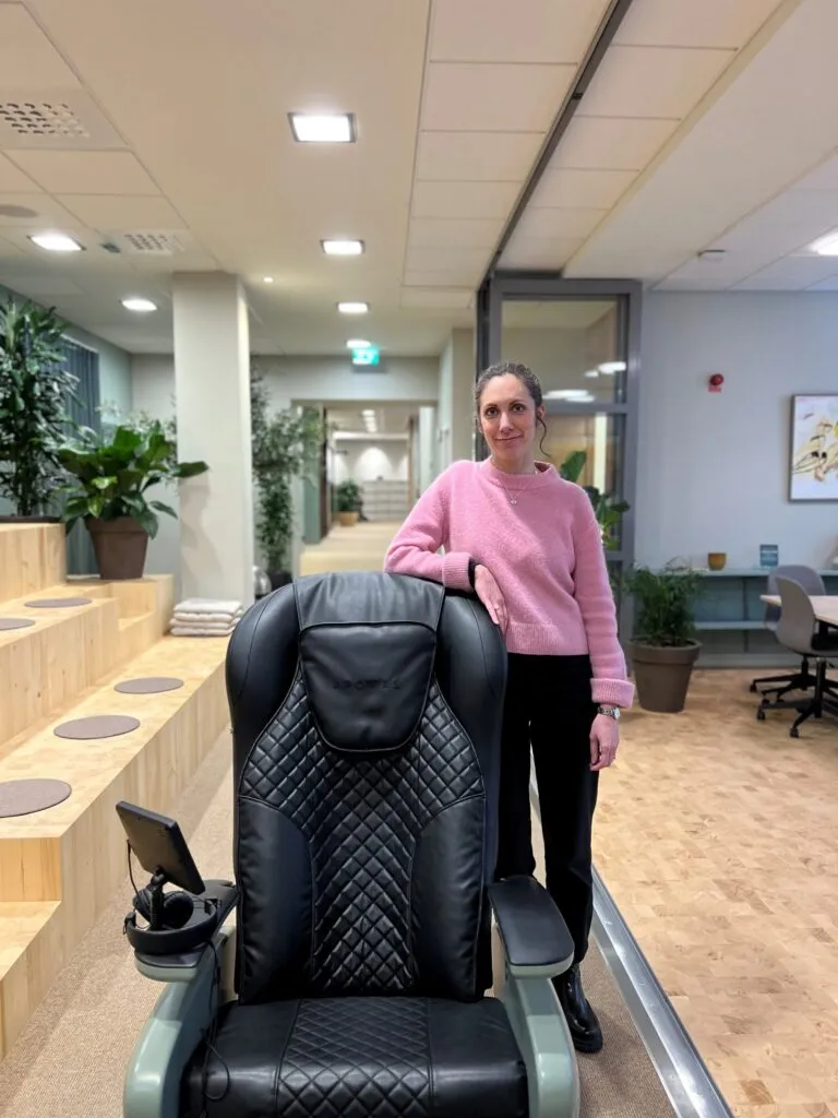 Kvinna som står bredvid en svart massagefåtölj hos Skandia Fastigheter