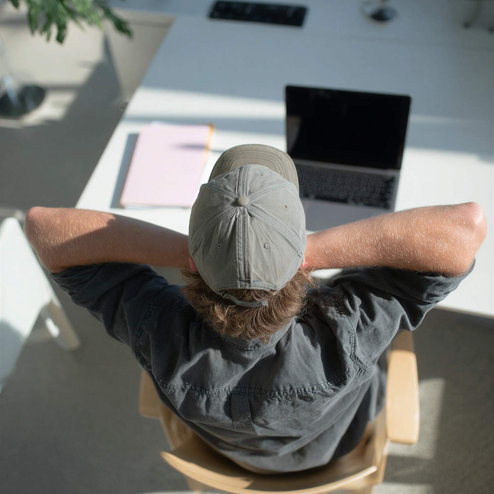 Person som lutar sig bakåt med händerna bakom nacken framför en laptop, sedd uppifrån