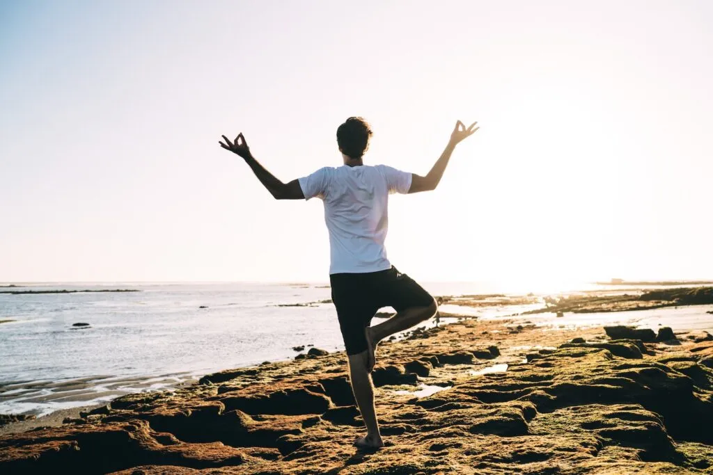 Person som står i yogaställning på en klippa vid havet