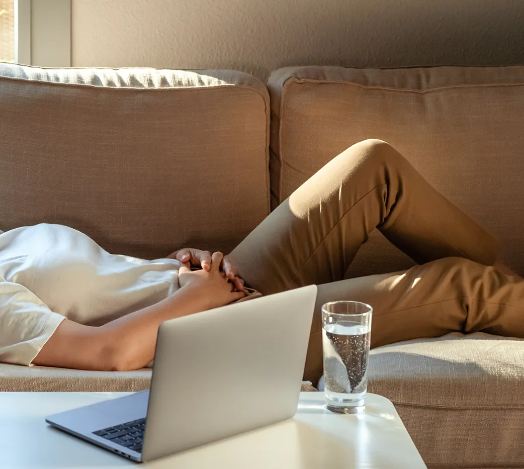 Person som ligger i soffan med laptop och ett glas vatten